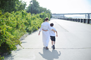 Mother and son walk along the waterfront, full length, rear view.