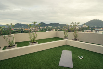 Obraz premium Morning yoga exercise concept. Mat on the green grass on the roof top with beautiful city view.
