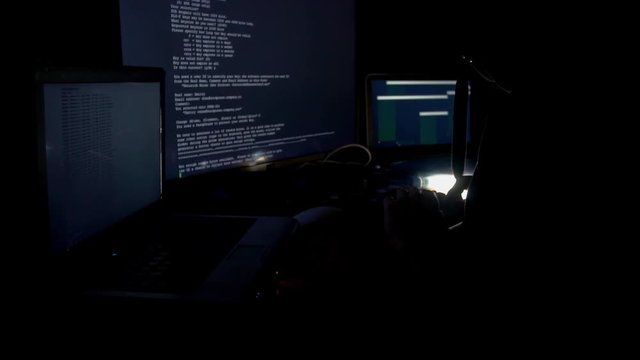 Hacker in hood cracking code using computers in dark room