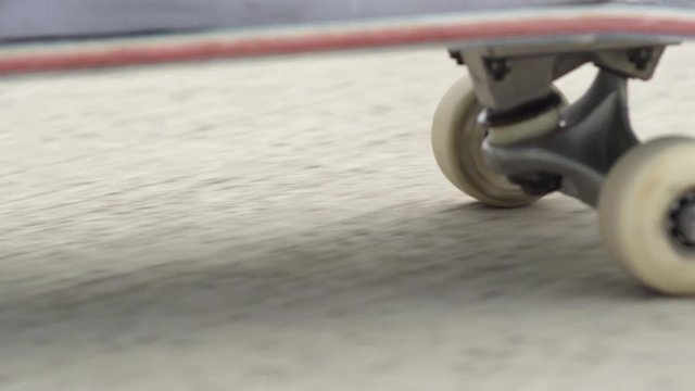CLOSE UP: Skateboard deck and wheels spinning along the concrete street