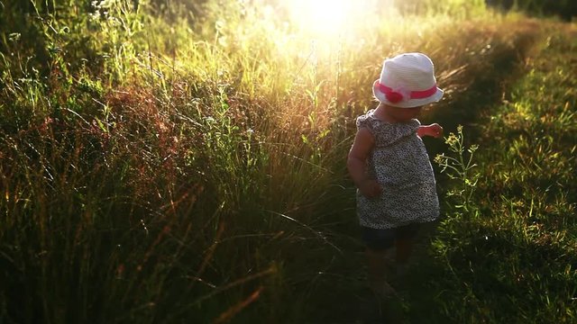 Little girl climbs on a glade in a beautiful sunset. child learns. Nature