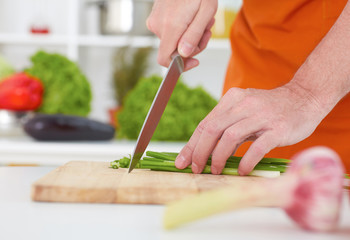 Obraz na płótnie Canvas Close up of unrecognizable man chopping green onion with kitchen knife on cutting board. Healthy eating, dieting, slimming and weigh loss concept.