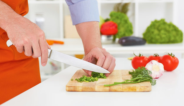 Mature man's hands  chopping onion on a wooden chopping board with knife.
