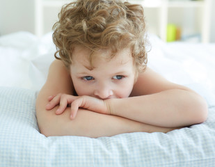 Portrait of pensive little boy lying on bed at the day time.