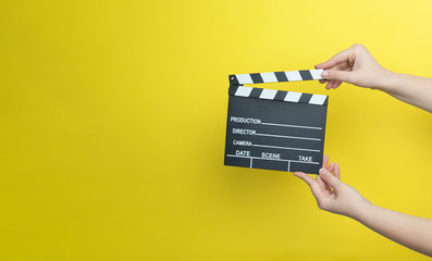 woman holding movie clapper on yellow background, cinema concept