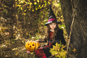 Happy Halloween. Cute little witch with a pumpkin in the hands.