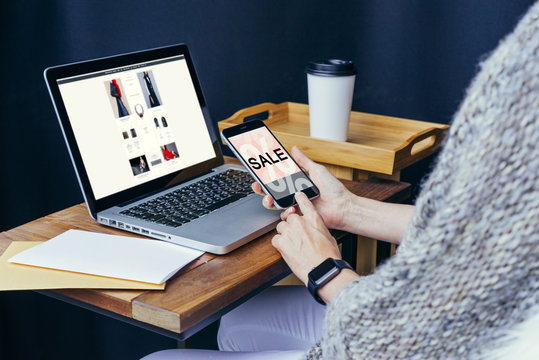Close-up of laptop on wooden table and smartphone with blank screen in hands of a girl. Next is letter and a gold envelope.On table is cup of coffee. Woman checks email on smartphone.Girl uses gadget.