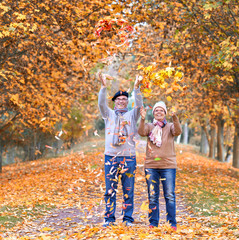 Fototapeta premium lachendes Seniorenpaar in einer Allee, Laub werfen im Herbst