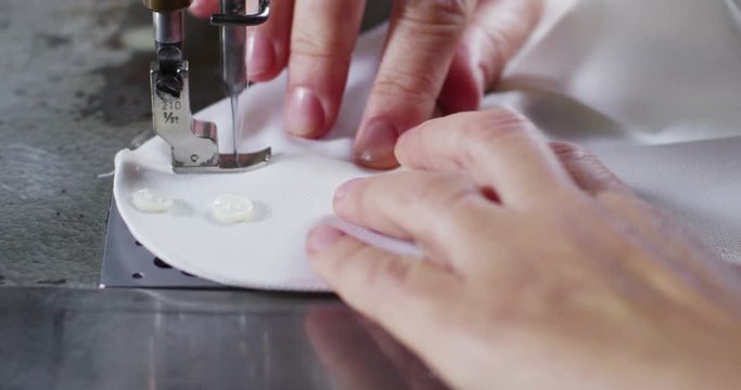A hand of a young seamstress sewing a white cloth tailoring according to the tradition of tailors. The dressmaker uses perfectly needle and thread to sew