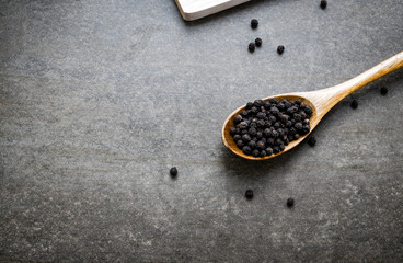 Milled black pepper corns on wooden spoon.