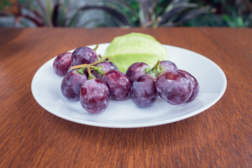 Grapes with water drops in a dish on table.