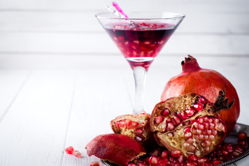 Pomegranate, cut into sections on a metal dish in the background of the shot glasses with red drink