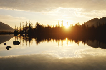the sun rises over the trees on a lake