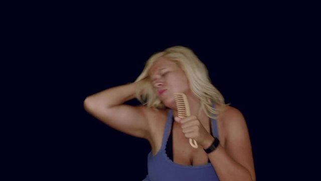 Funny blond woman dancing and singing with comb, studio isolated.