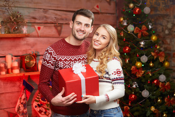 Obraz na płótnie Canvas Happy Couple in winter sweaters smiling and holding big red gift box