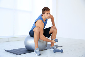 Fototapeta premium Young man doing exercises with dumb-bells and ball on rug