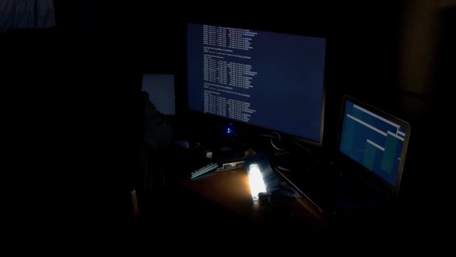 Hacker in hood cracking code using computers in dark room