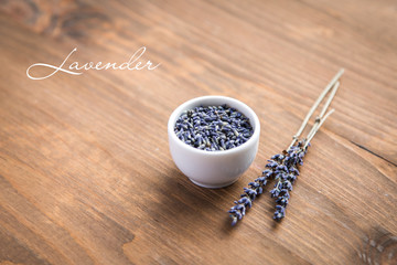 lavender flowers in small bowl with sprig on wooden background