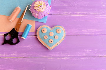 Felt heart decorated with buttons. Sewing supplies on colorful wooden background with empty place for text. Sewing project for Valentine's day, wedding, mother's day. Top view