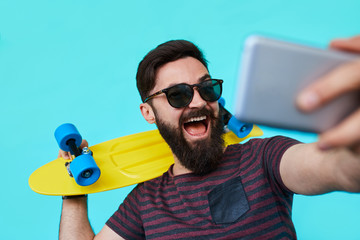 young man in casual clothes make selfie with his bright skateboard