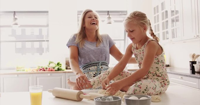 Girl sitting on kitchen counter with bread dough beside excited mother having fun
