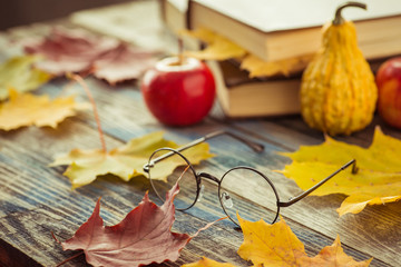 Eye glasses with book and autumn leaves on table