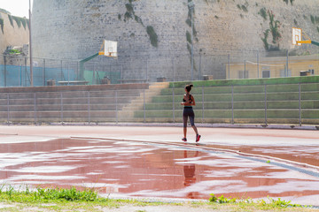 Woman runner jogging on wet red run lane at stadium. 