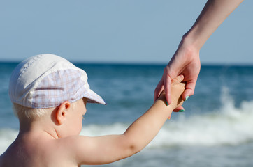 Little blond boy in a cap holding my mother's hand on the background of the sea, view from the back