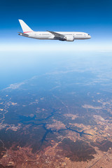 Podróż samolotem, samolot lecący w błękitnym niebie wysoko nad ziemią - obrazy, fototapety, plakaty