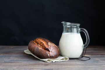 Black rye bread and jug of milk on wooden table. Copy space. 