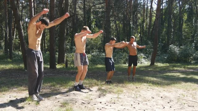 Group of athletes warming up his body and hands before training in the forest. Young strong muscular men stretches before workout at the nature. Sportsmans doing exercise at the wood outdoor. Close up