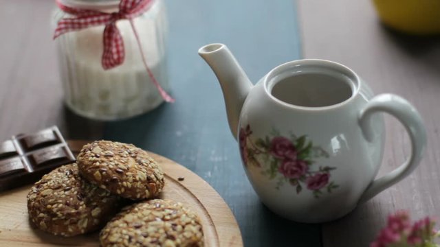 Preparation of black tea in the kettle. Pour hot tea in a white ceramic Cup with a saucer. Wooden table, biscuits, sugar.