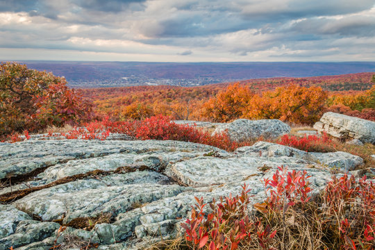 Vibrant fall foliage grow along granite rocks under a dramatic sunset at the top of New Jersey at High Point State Park