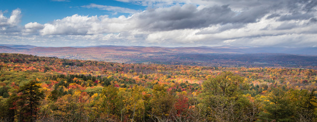 A scenic overlook displays brilliant fall foliage under bright and cloudy sky in the Catskill Mountains in New York