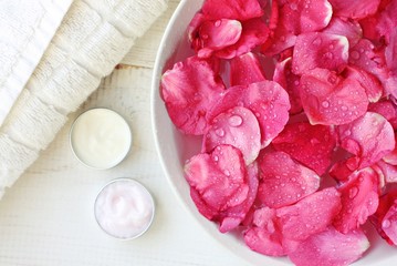 Aroma spa skincare treatment. Rose petals in bowl, body care moisturizers, white towel. Pampering beauty routine. 