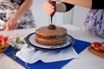 Two girls making a cake on the kitchen. Female hand squeezes the chocolate cream