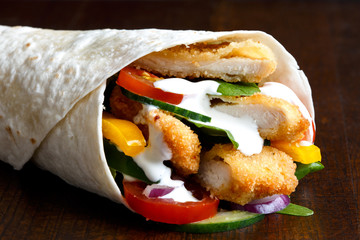 Detail of crumbed fried chicken and salad tortilla wrap with white sauce.