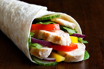 Detail os grilled chicken and salad tortilla wrap on dark background.