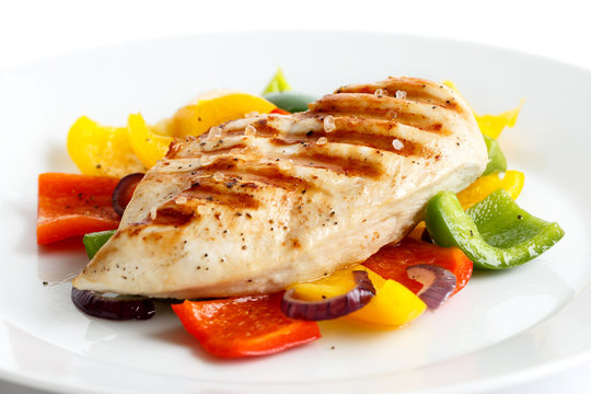 Plate of whole seasoned grilled chicken breast on roasted peppers.
