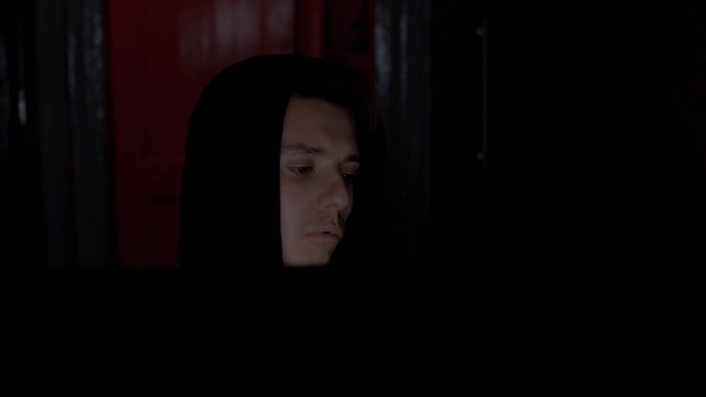 Criminal programmer in hood cracking code using computers in dark room