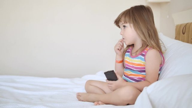 Adorable child in colourful dress watching tv on the bed