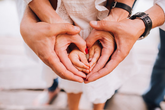 A family of hands form a heart - father on the outside, then mother's hands and infant baby hands in the middle.