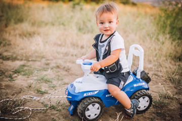 Funny boy car driver with the steering wheel. year-old boy in a white shirt in a red toy car in the street. Little boy driving big toy car and having fun, outdoors. Young kid portrait with toy car