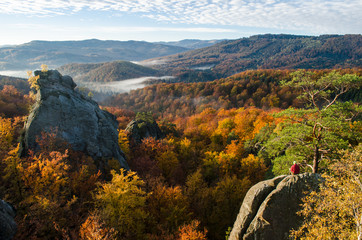 Man sitting on the rock and watching the colorful autumn landscape around him
