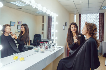 Make up artist doing professional makeup of young woman near the mirror in beauty studio