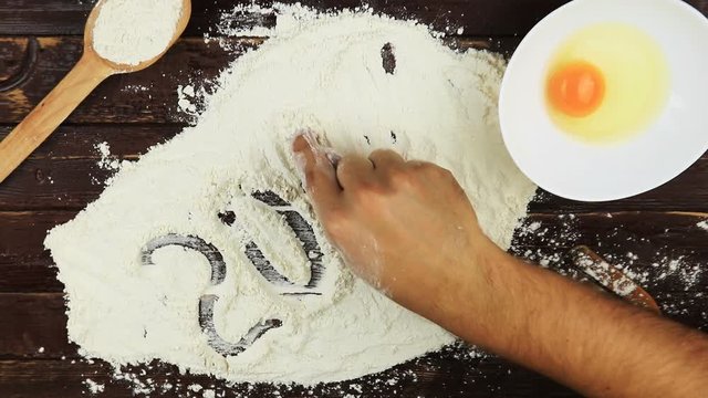 Top view Young man writes a word number 2017 on white flour at wooden desk from above.