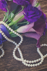 Bouquet of fresh calla lilly and eustoma flowers with pearls close up on wooden table, retro toned