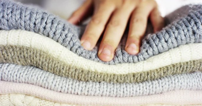A hand touching a pile of colorful wool sweaters warm fluffy soft and comfortable to wear. cleaning concept, softness, warmth, cashmere, whiteness.