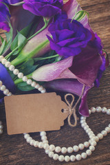 Bouquet of calla lilly and eustoma flowers on wooden table with empty paper note, retro toned