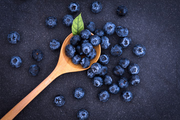 fresh picked blueberries in wooden spoon on black stone background